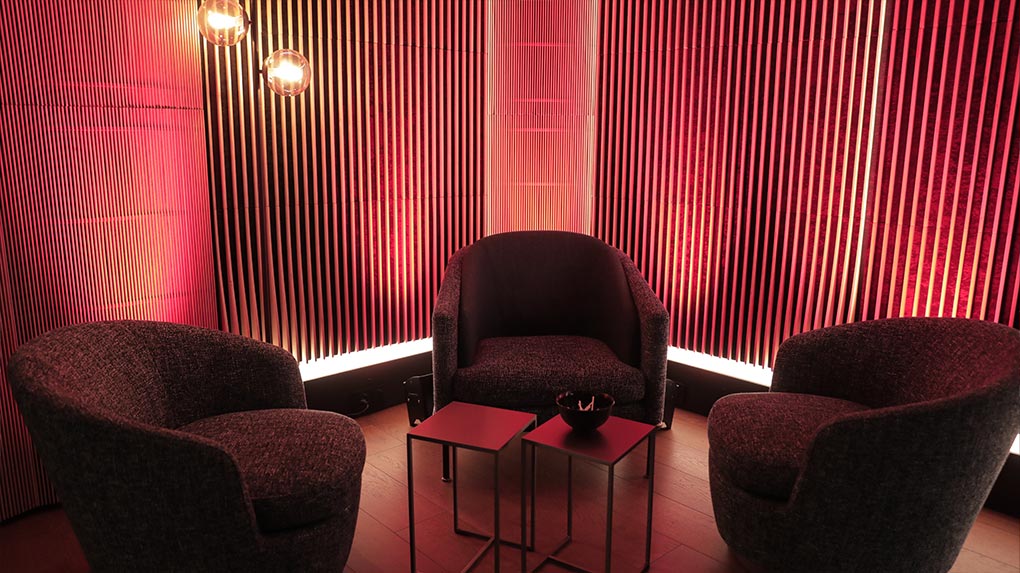 Coin fauteuils avec trois fauteuils, tables basses et éclairage rouge sur un mur à lattes verticales.