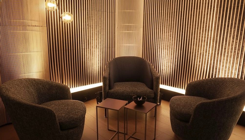 Coin fauteuils avec trois fauteuils, tables basses et éclairage neutre sur un mur à lattes verticales.